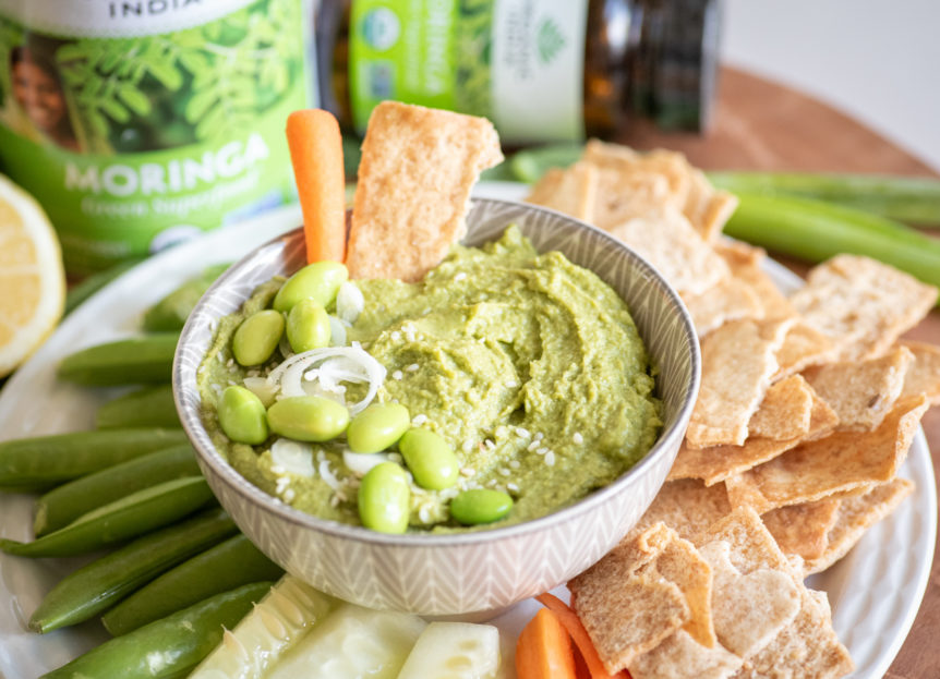 Spinach moringa edamame dip in bowl with raw veggies and chips for dipping.