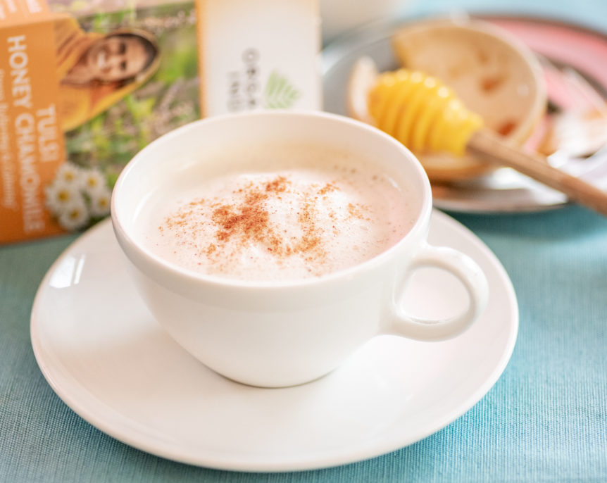 Tulsi Honey Chamomile Latte topped with cinnamon in a white teacup with saucer.