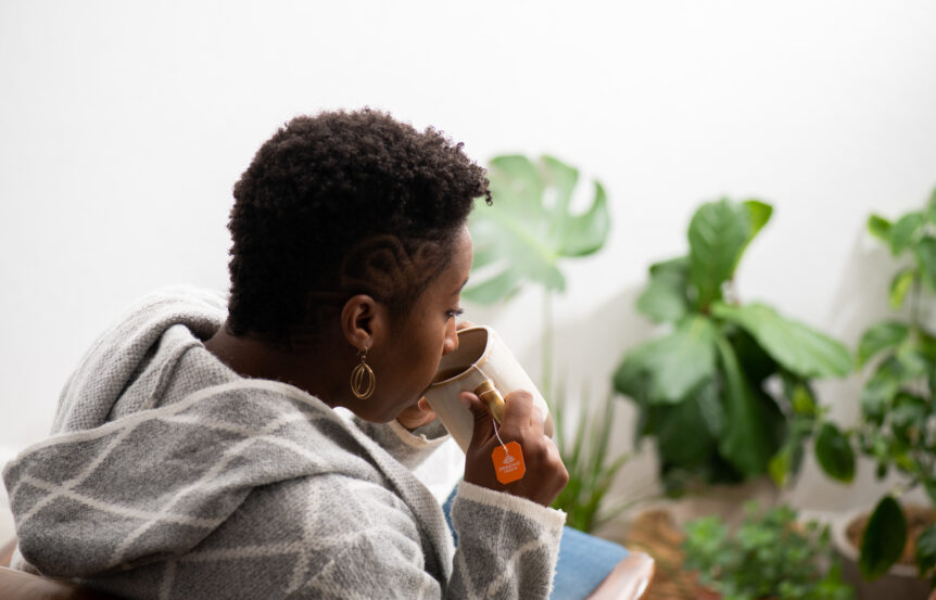 Woman drinking tulsi turmeric ginger tea, herbs for lymphatic drainage, from a tea mug with lots of plants surrounding.