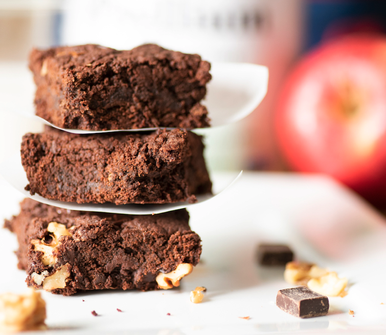 A stack of vegan fudge brownies on a white plate with walnuts.