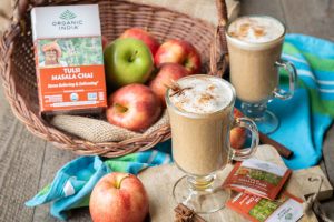 apple chai latte with a basket of apples and organic india tulsi masala chai tea.
