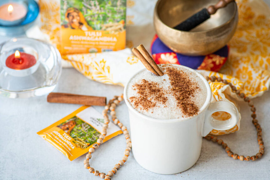 Ashwagandha latte in a white tea cup with fresh cinnamon on marble table with mala and tea bags.