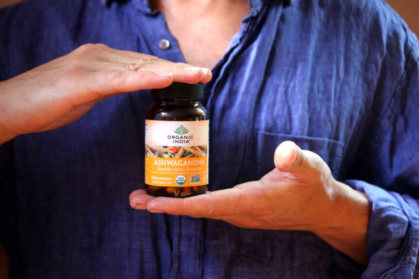Man with blue shirt holding glass ashwagandha capsule jar, as herb for cortisol balance.