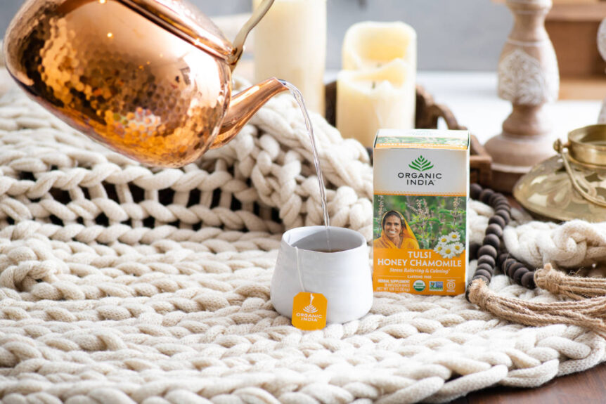 benefits of chamomile tea with cozy blanket, copper pot and teacup full of chamomile tea.