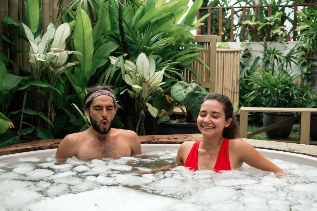 Couple cold plunging in an ice bath surrounded by greenery