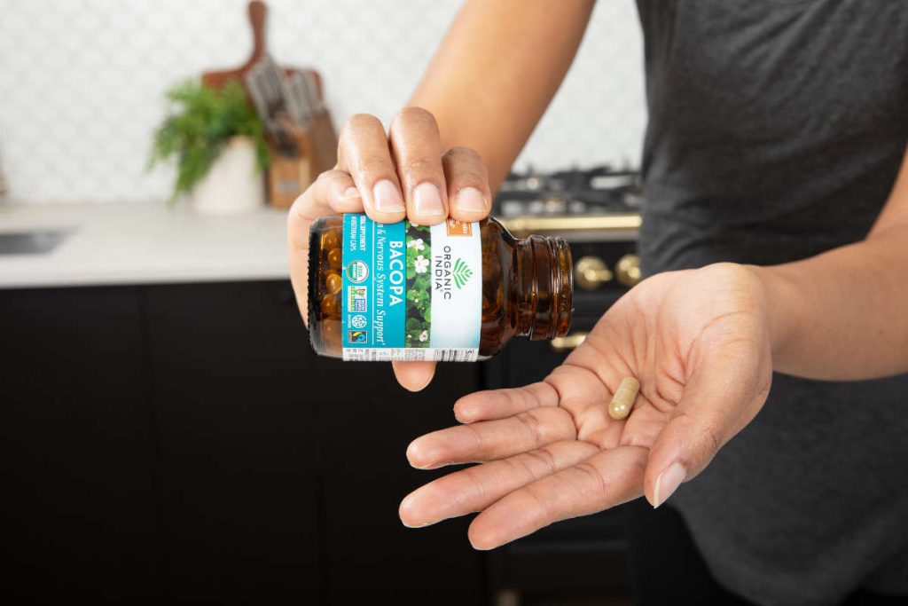 Woman taking bacopa capsules, an herb for biohacking brain health