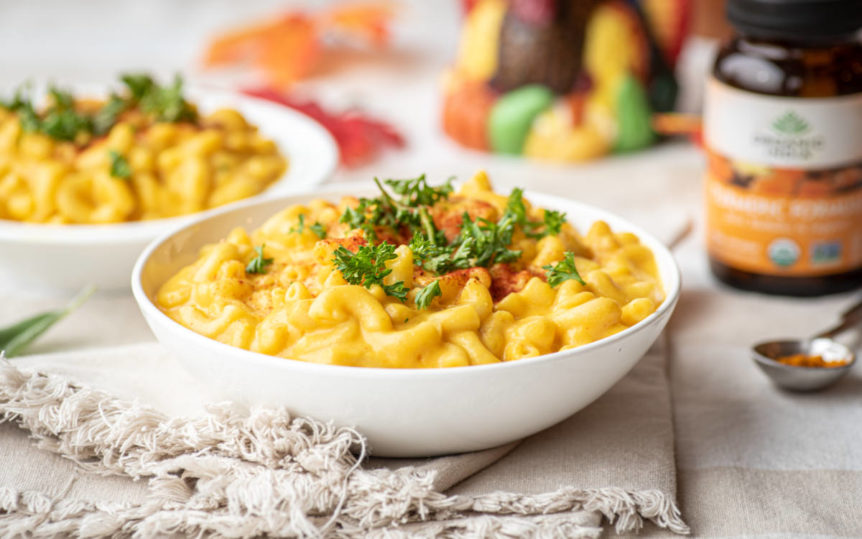Bowl full of creamy butternut squash mac n cheese with a spoon of Turmeric nearby.
