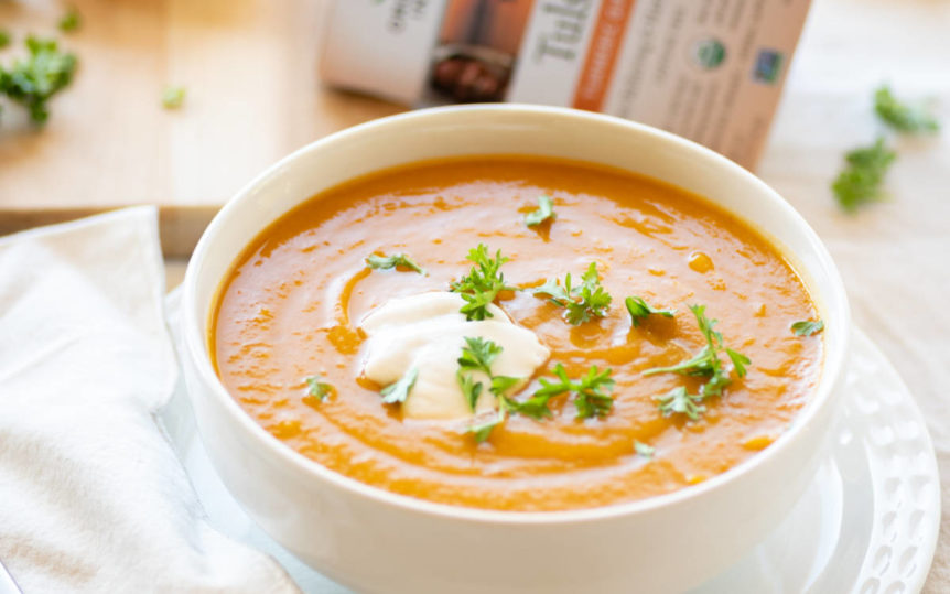 White bowl full of carrot sweet potato soup with a dollop of vegan cream.