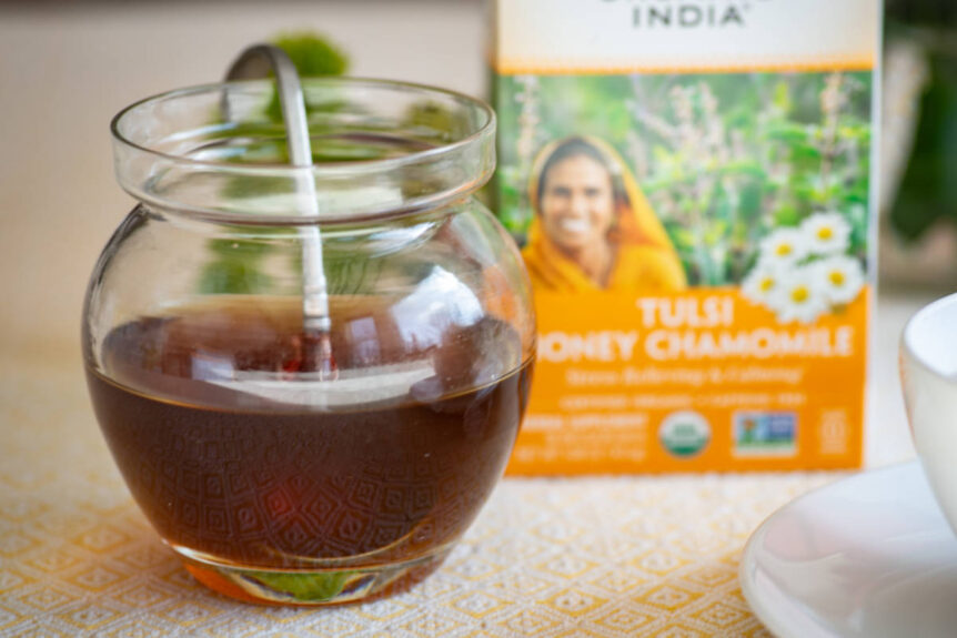 Chamomile syrup in a glass aw on a wood table with box of chamomile tea beside it.