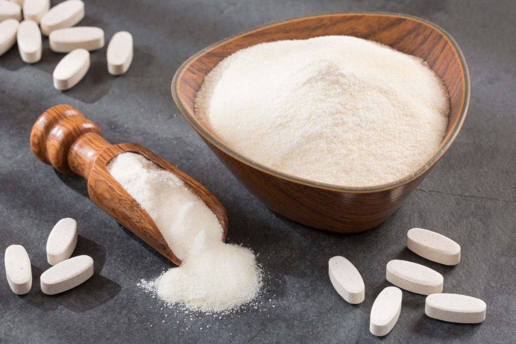 Collagen powder and pills on table in wooden bowls