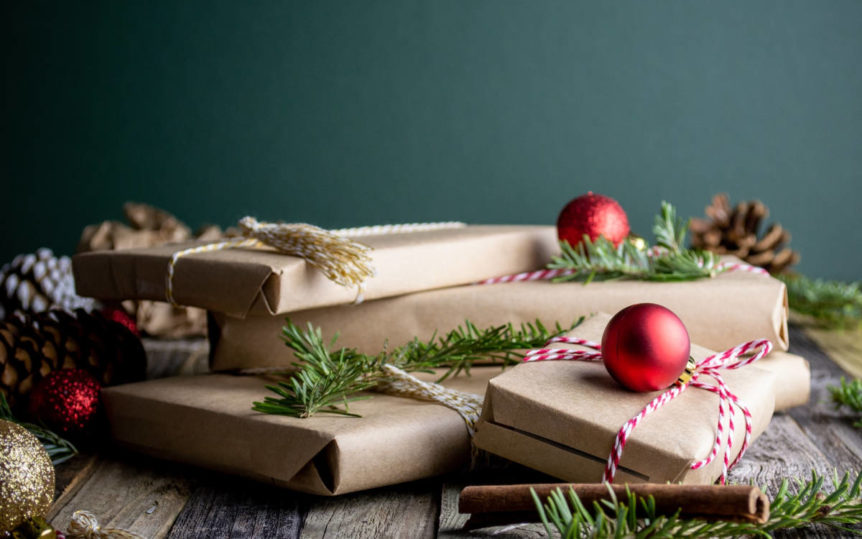 Pile of gifts wrapped in neutral brown shipping paper with pine sprigs after conscious holiday shopping.