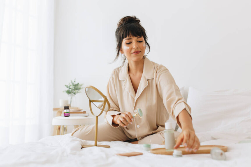 woman applying herbal face mask for dry skin in bed in PJs