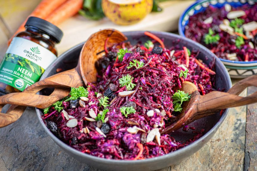 Glow beet salad with neem in a bowl with wooden serving spoons.