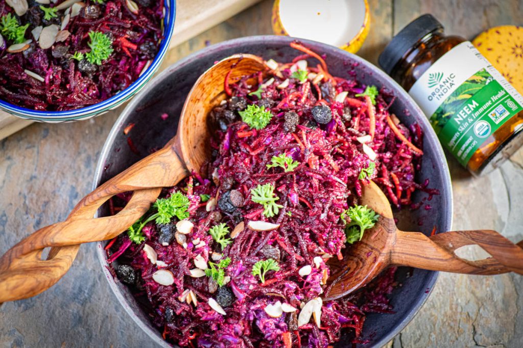 Glow beet salad with neem in a bowl with wooden serving spoons.