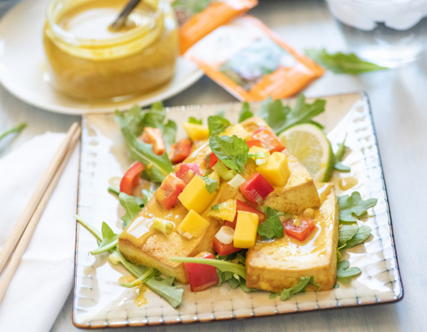 Coconut ginger marinade on tofu with fresh veggies on a bed a greens.