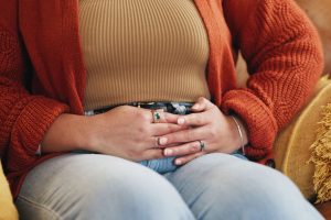 Woman with hands to lower belly in jewel toned autumn sweater tending to gut and immune health