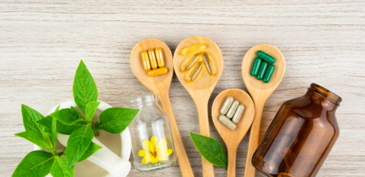 Multiple supplements for herbal pairings on a wood table with wooden spoons.