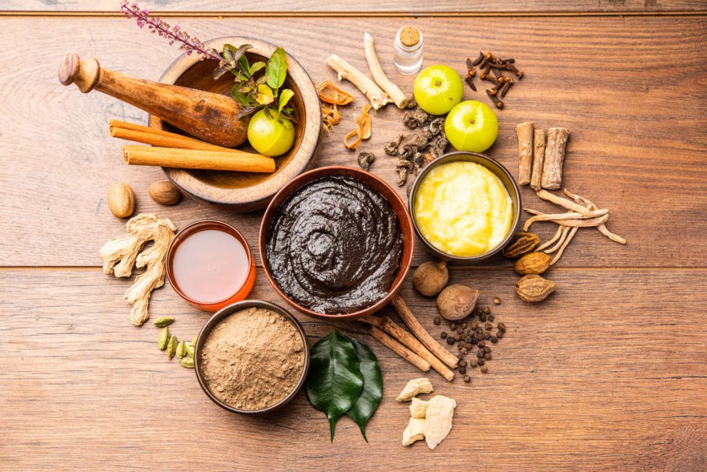 Herbs for cortisol in Ayurveda like Amla, Ashwagandha, Tulsi and more on a wood table.