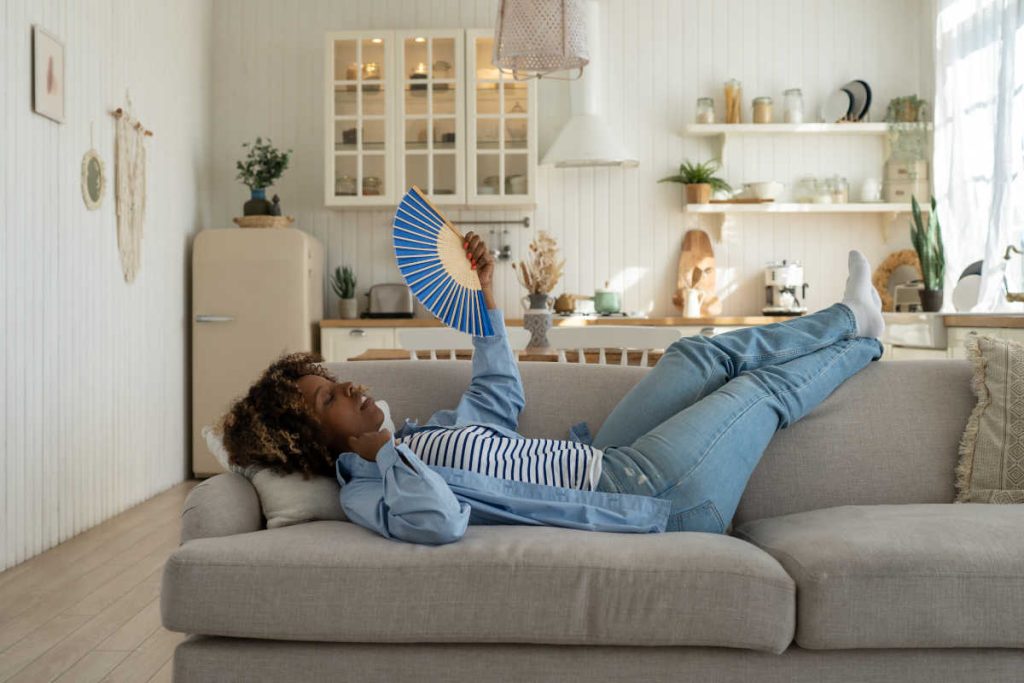 Woman on couch with hand fan, needs herbs for hot flashes.