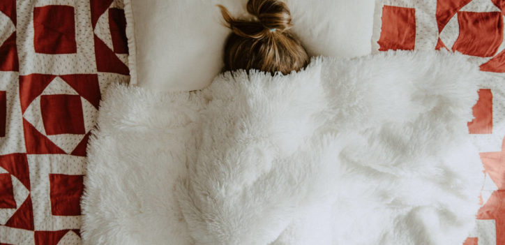 Girl in bed with cover over her face and hair in bun recovering with herbs for immunity.