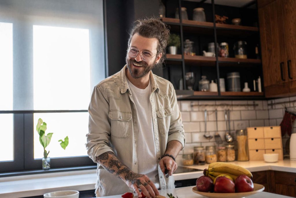 Man in kitchen smiling while cutting up fruits for health and wellness.