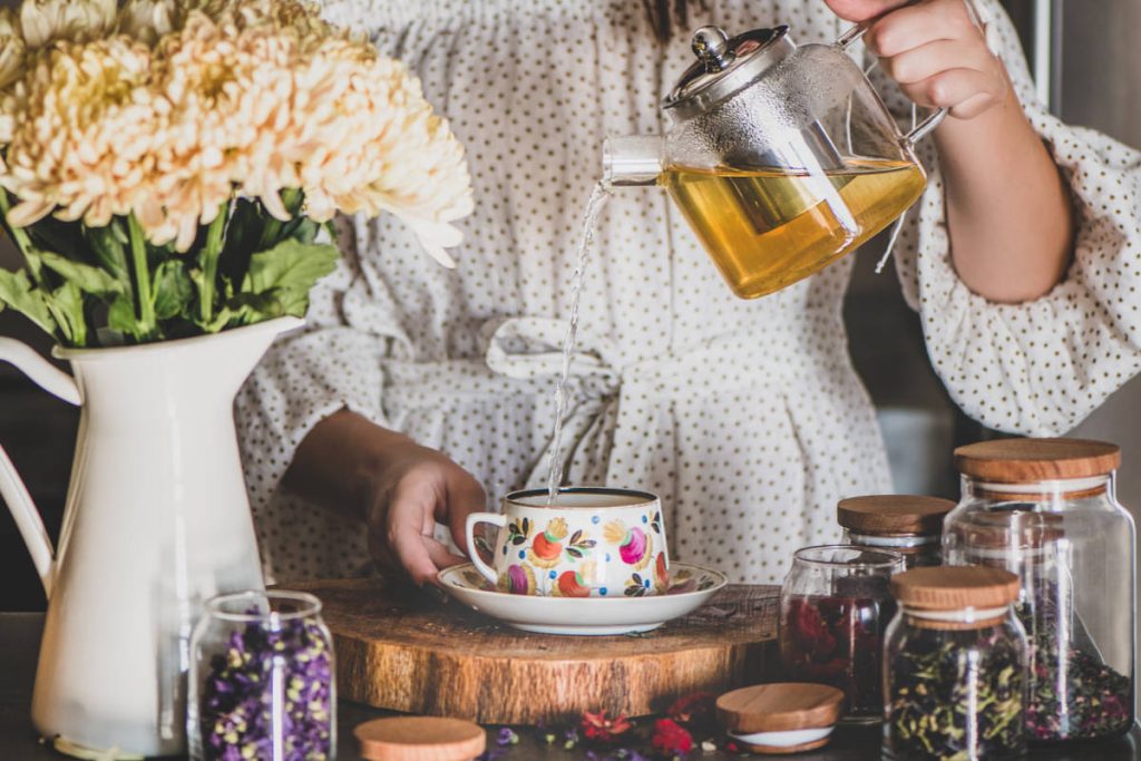 Women in polka dot dress pouring tea with herbs for the zodiac, practicing astroherbalism from home.