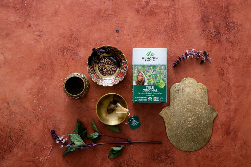 Tulsi Tea on burnt orange color table with hamsa, metal bowls and fresh Tulsi.