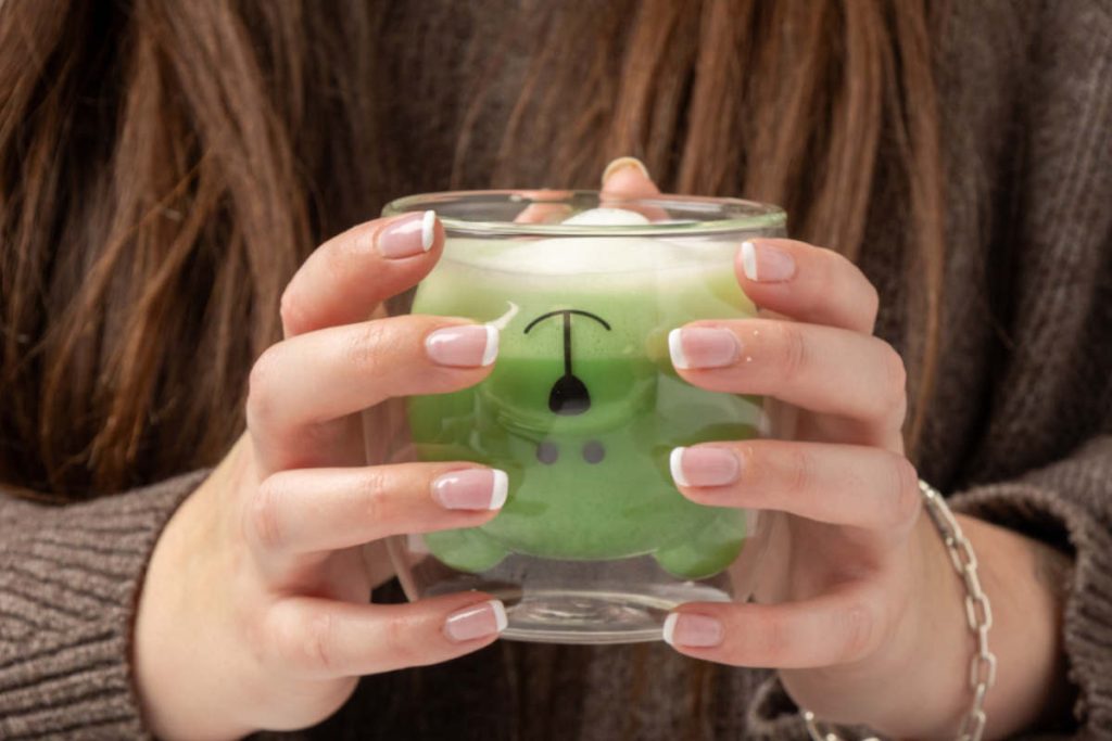 woman holding matcha moringa latte in bear mug
