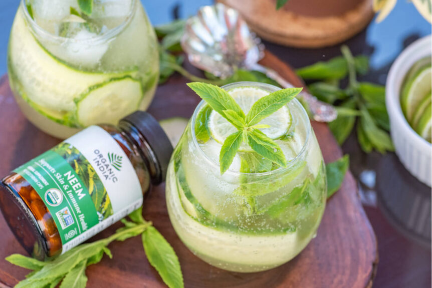 Neem Beauty Spritzer in a glass on wooden platter garnished with mint, lime and cucumber.