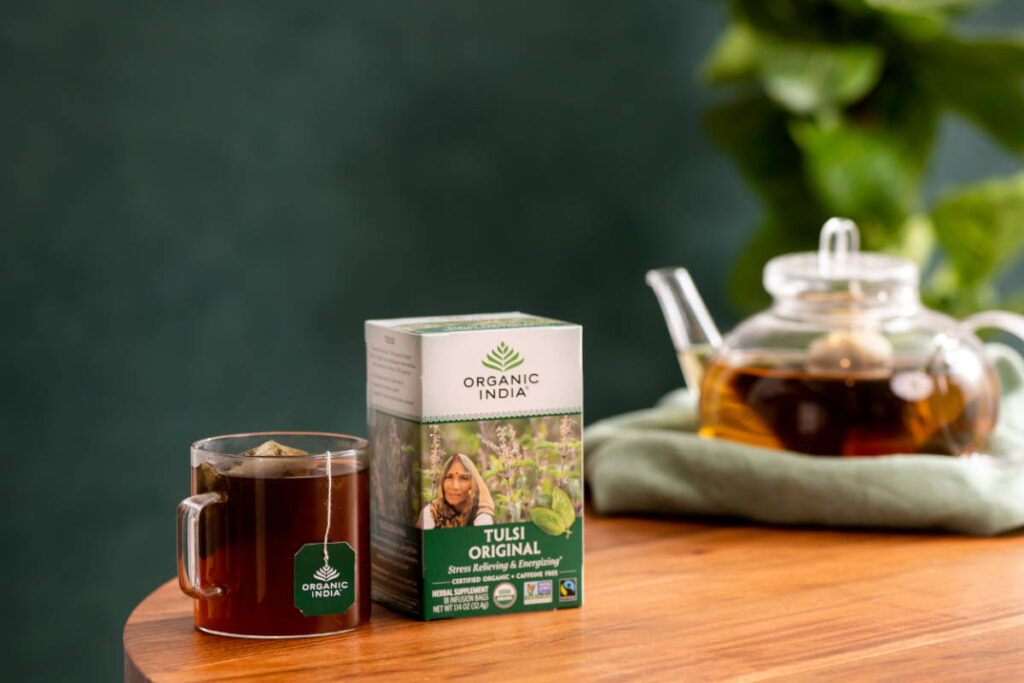 Nervine herb tulsi prepared as tea in clear teacup and infuser pot on wooden table.