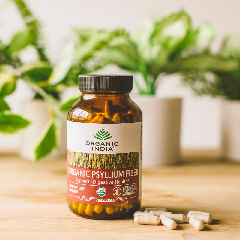 Psyllium fiber capsule on wooden table with plants in the background.