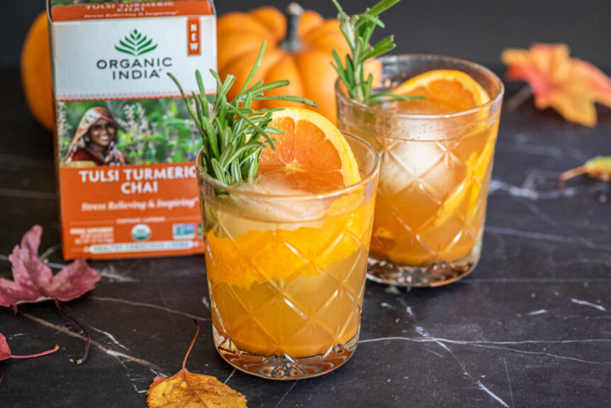 Pumpkin old fashioned mocktail with rosemary and orange garnish and sugar spice rim in clear glass.