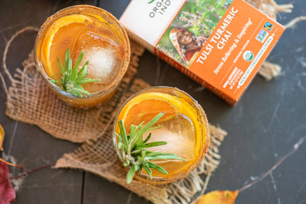 Pumpkin old fashioned mocktail with rosemary and orange garnish and sugar spice rim in clear glass.