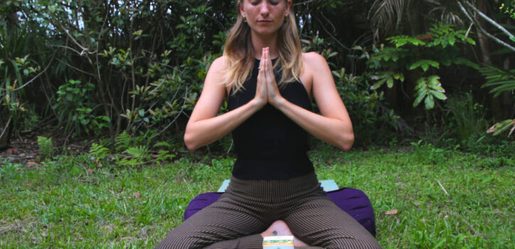 Woman sitting in meditation with tea on a yoga mat outside in nature