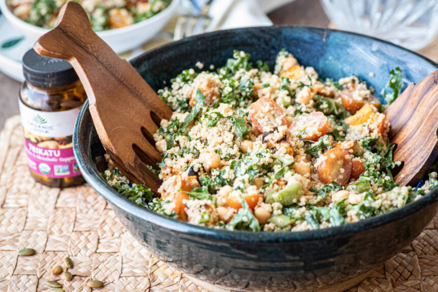 Kale Quinoa salad in salad bowl with salad servers and trikatu dressing.