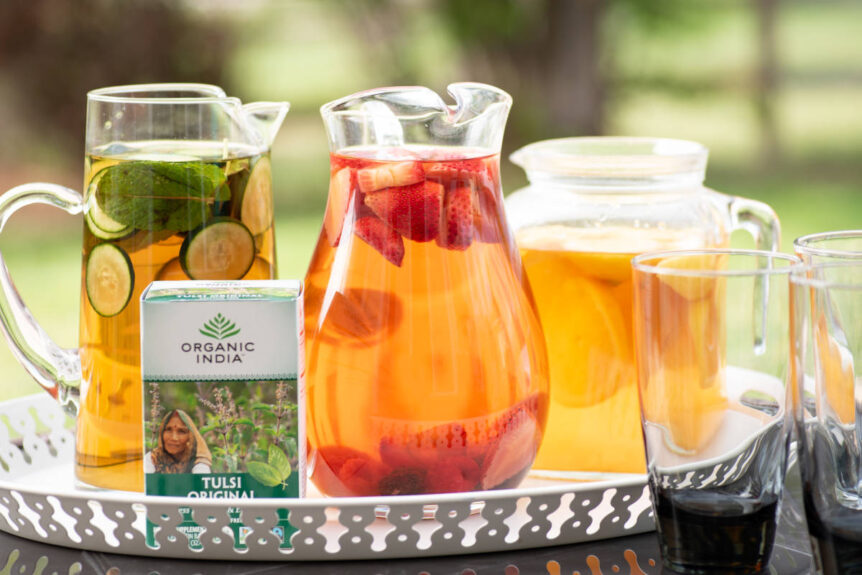 Tulsi cold brew (holy basil iced tea) in pitchers with different garnishes like strawberry, cucumber, mint and lemon.