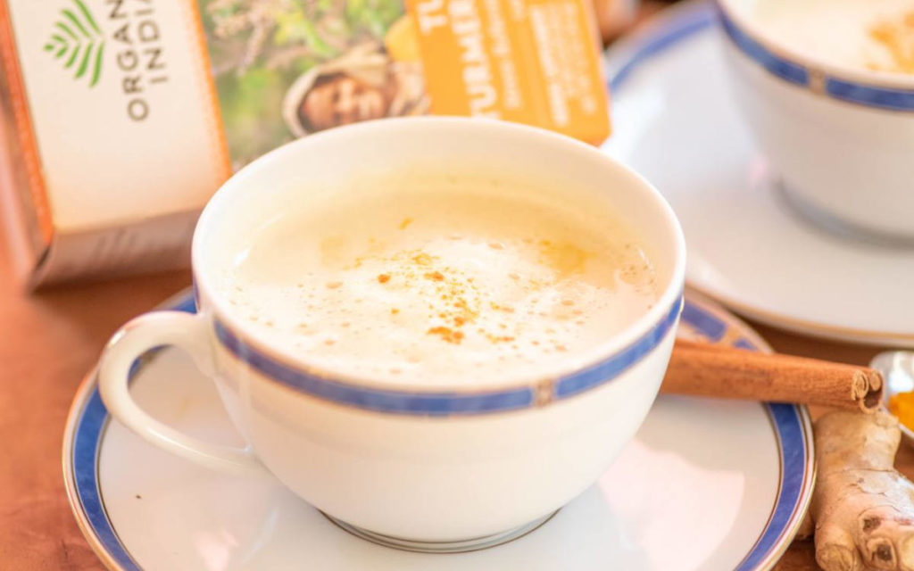 A cup of turmeric golden milk latte in a white and blue teacup with ginger and cinnamon.