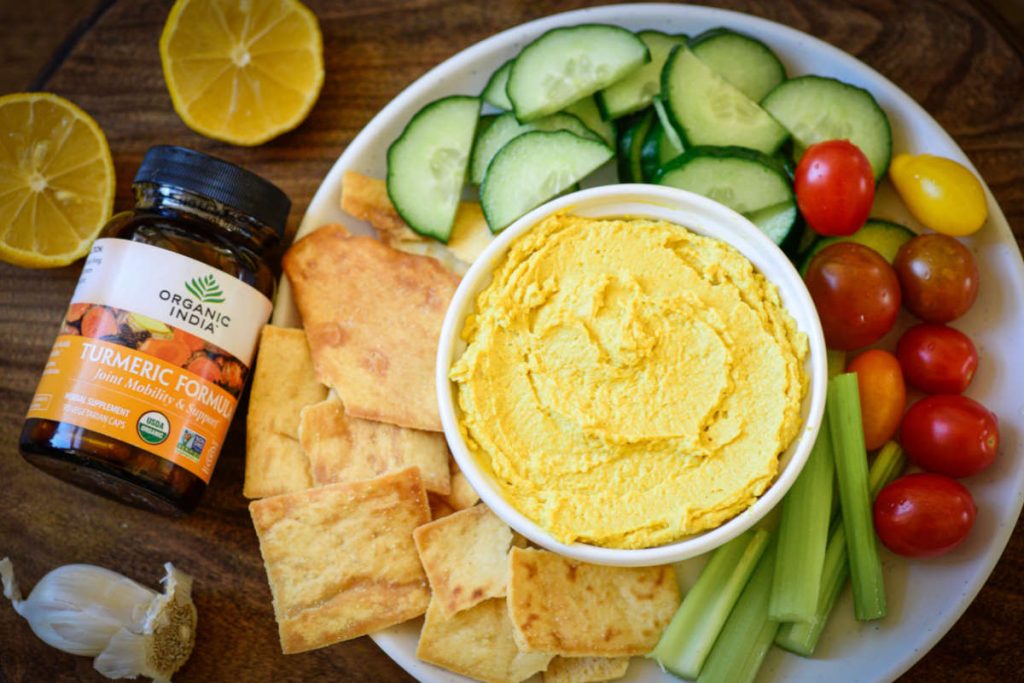 Turmeric Hummus in a bowl with pita chips and fresh veggies on the side