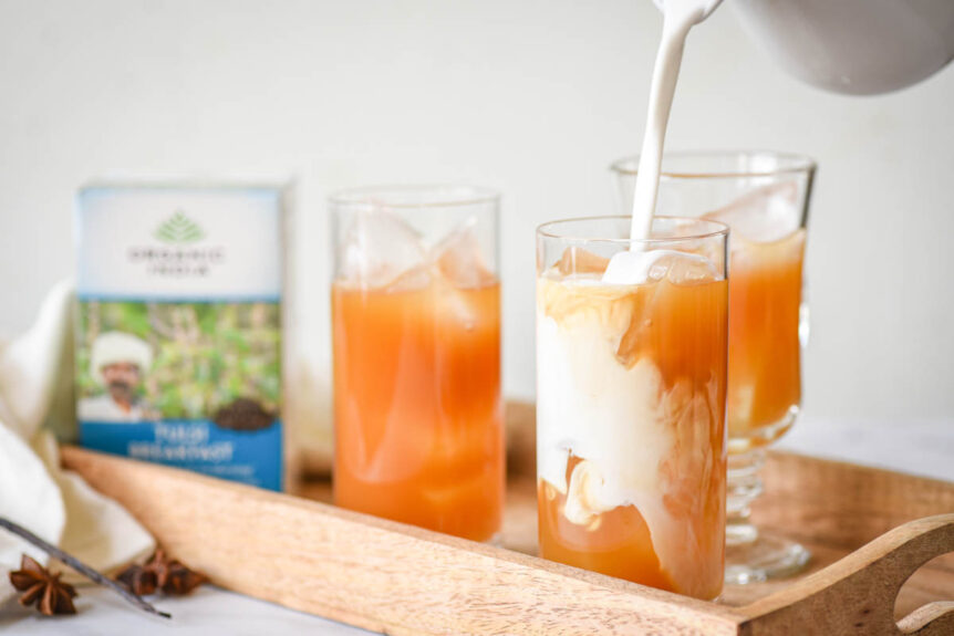 Thai Iced Tea in clear glass on wooden platter with coconut milk